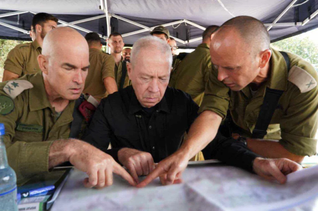 صورة تظهر 3 قادة اسرائليين اثناء التخطيط لما يبدو انه عمل عسكري وهم يتصفحون خريطة وبخلفهم عدد من الجنود في احد المخيمات او المعسكرات