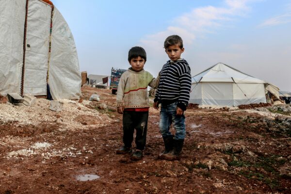 Two children standing in a muddy Syrian refugee camp in Idlib.